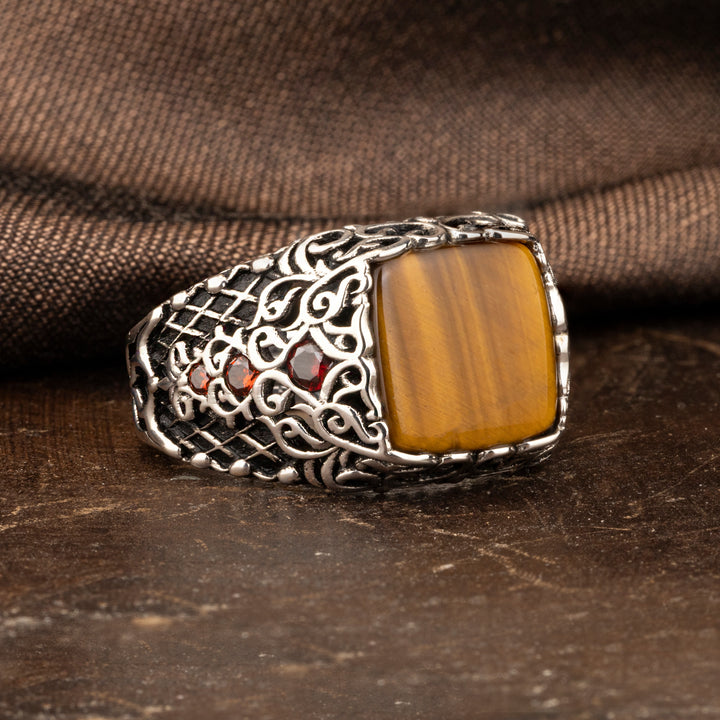 Square Tiger eye stone ring with small red  zircon stones on inlaid sides  on brown ground and brown silk background 