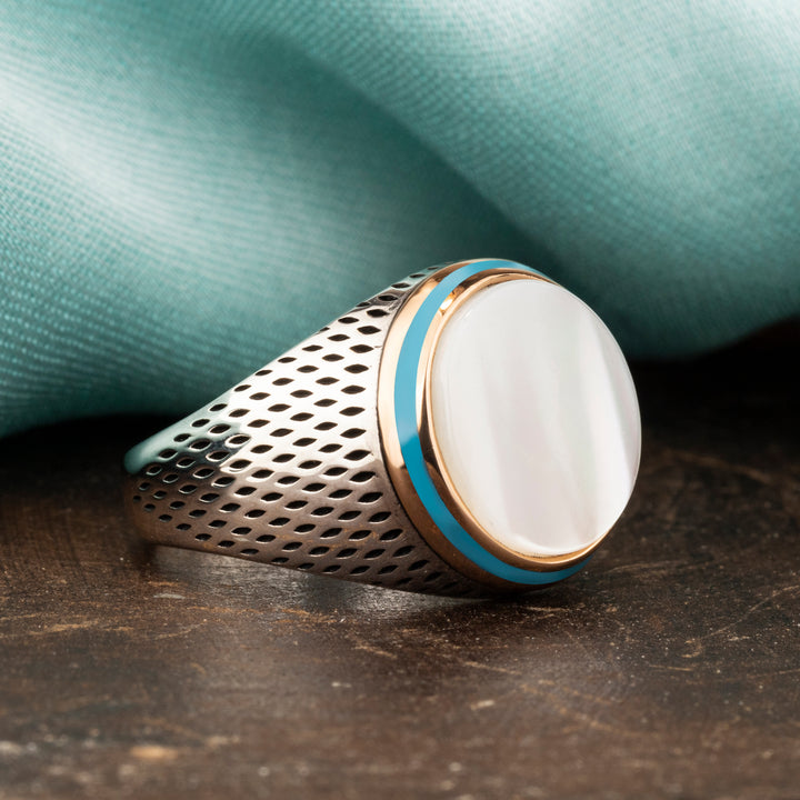 White Mother of pearl circled blue and gold line ring has a  small holes on the sides with the blue silk background and brown ground  